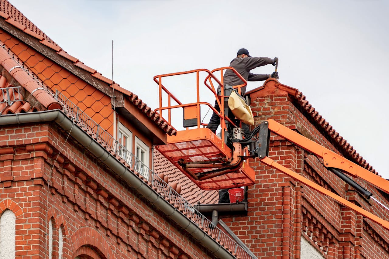 services-01 Roofer in a cherry picker conducting maintenance on a red brick building with a tiled roof.