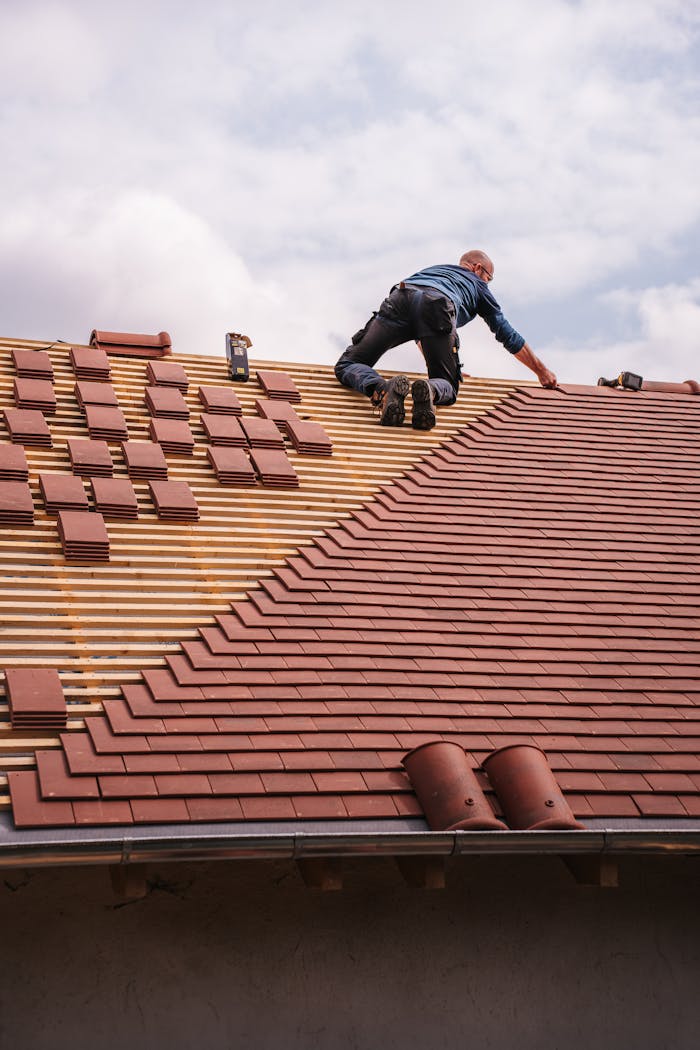 who-we-are A roofer carefully installs shingles on a new residential roof under a cloudy sky.